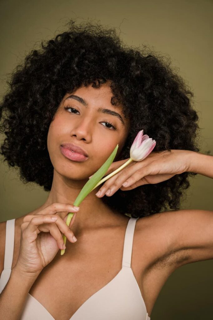 Gorgeous woman with curly hair holding a rose, exuding confidence and soft feminine energy.