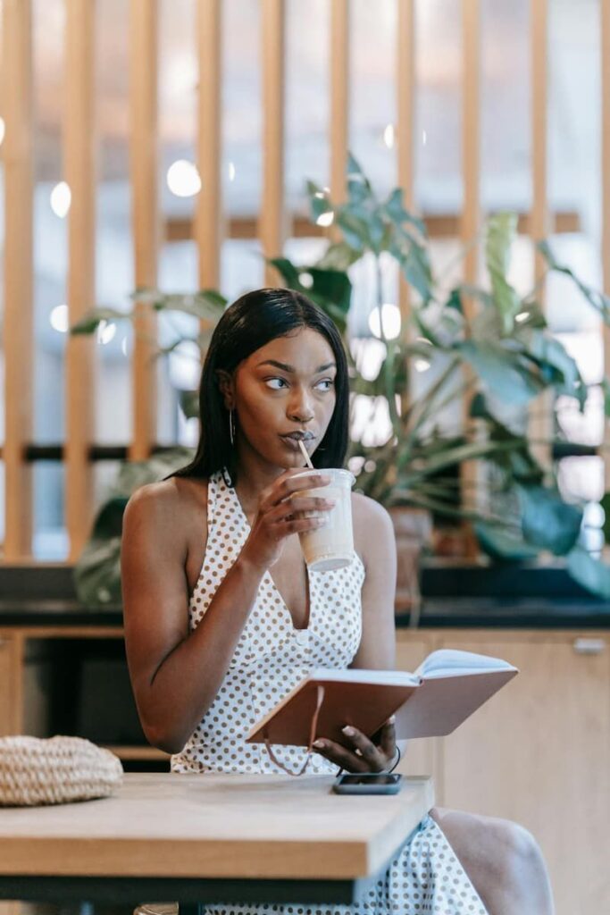 Woman in a cafe drinking coffee, holding her journal and doing manifestation scripting.