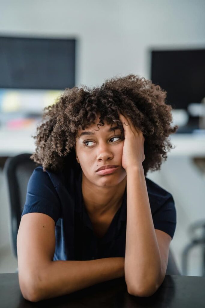 A frustrated woman wearing a black t-shirt holding her head because she's experiencing manifesting blocks.