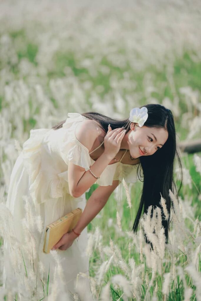 A woman in the field wearing a white dress and flowers in her hair, looking happy and content, represents manifesting using feminine energy.