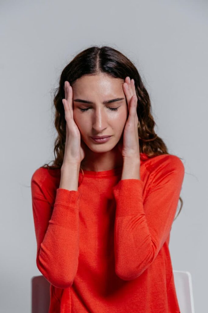 Image of a woman wearing a red t-shirt holding her head with both hands in frustration, signaling the need for a mid-year life reset.