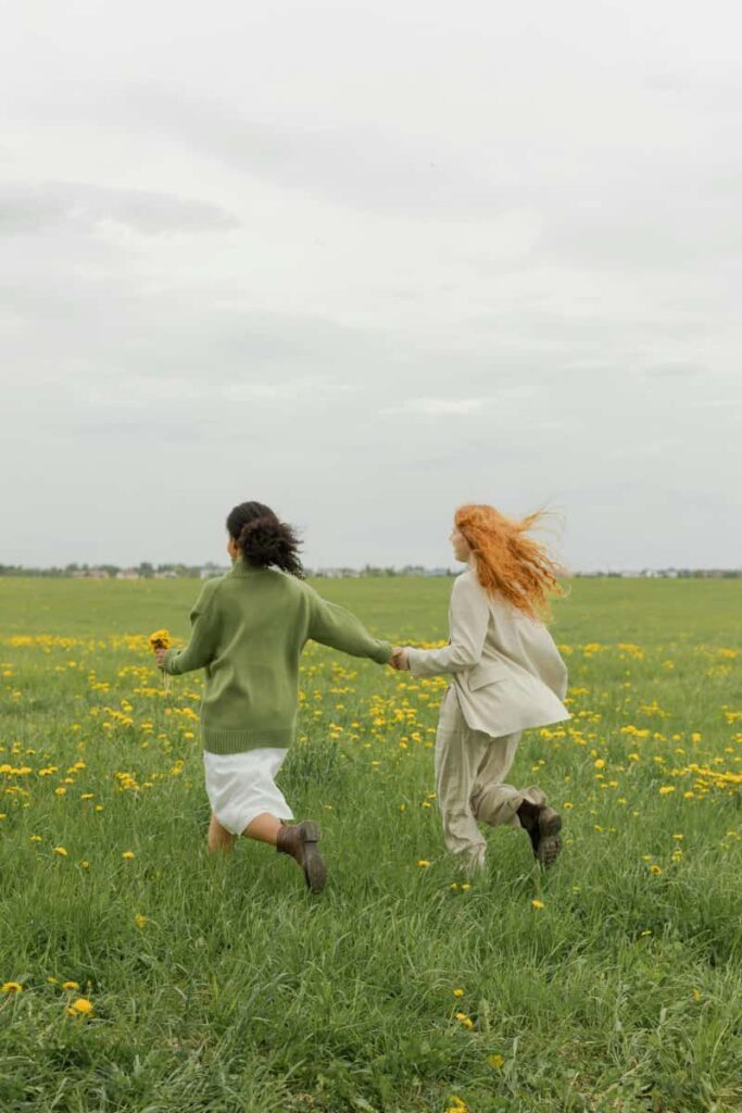 Two female friends holding hands and running on a green field.