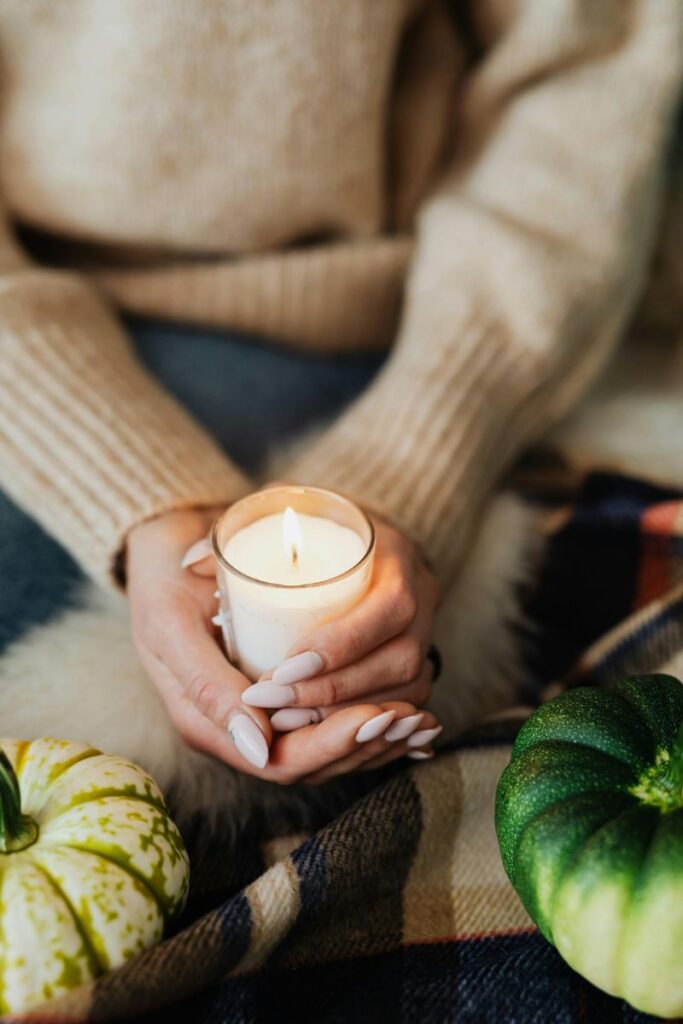 A woman with a beige sweater and pink nails holding a candle representing soft, feminine habits.