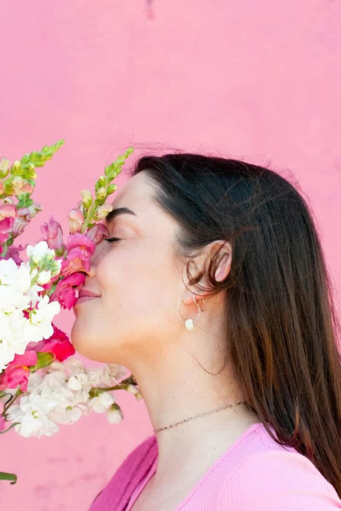 A woman in a pink sweater smelling a bouquet of white and pink flowers, signifying feminine energy microhabits.