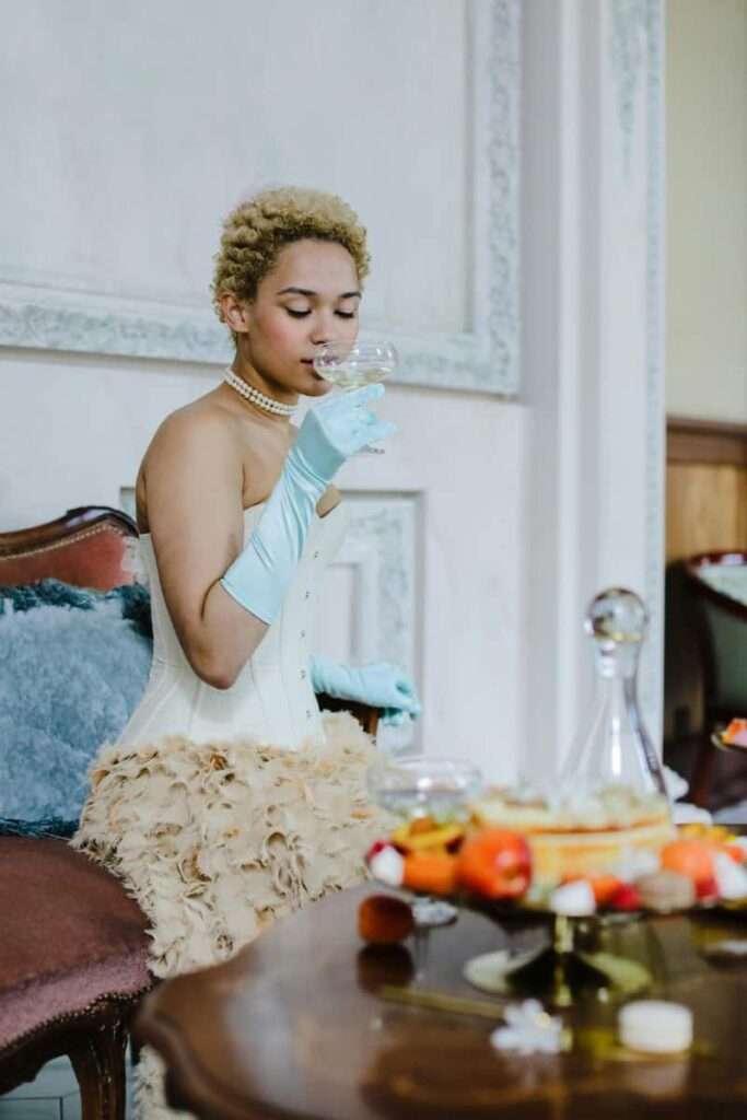 Image of a woman in a white and pink corset dress sipping champagne as a way to reinforce personal development through reward.  