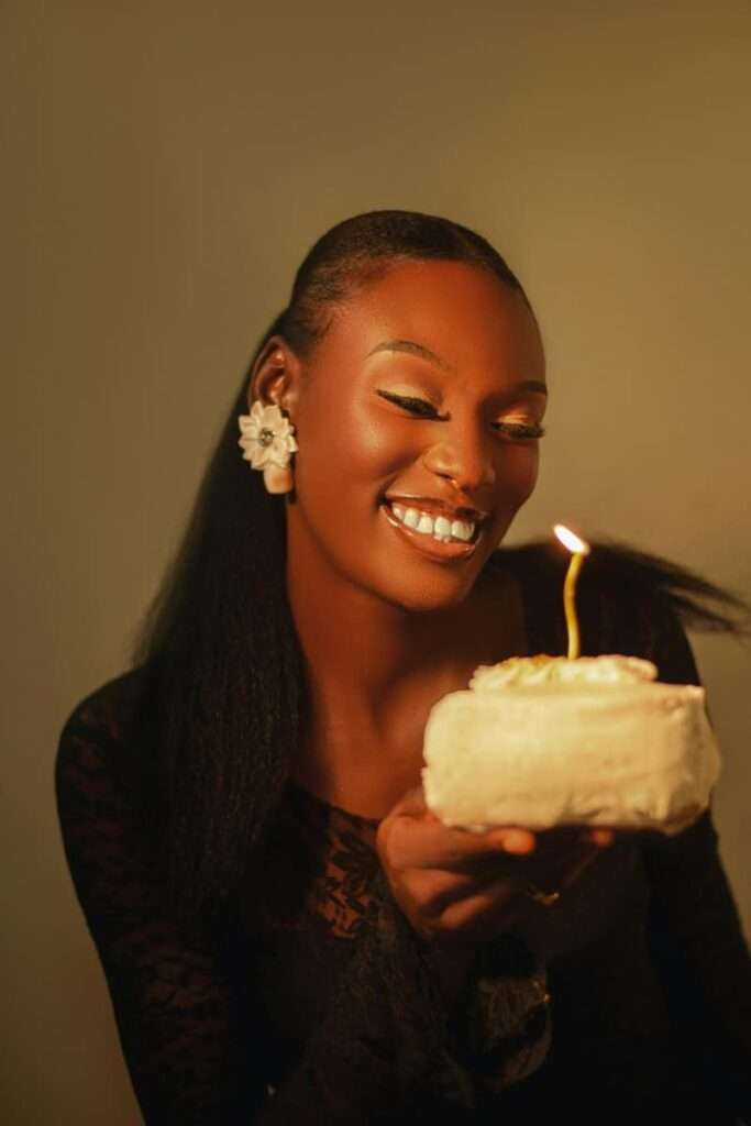 Image of a woman in black holding a birthday cake with a candle representing the benefits of using birthday reflection questions.