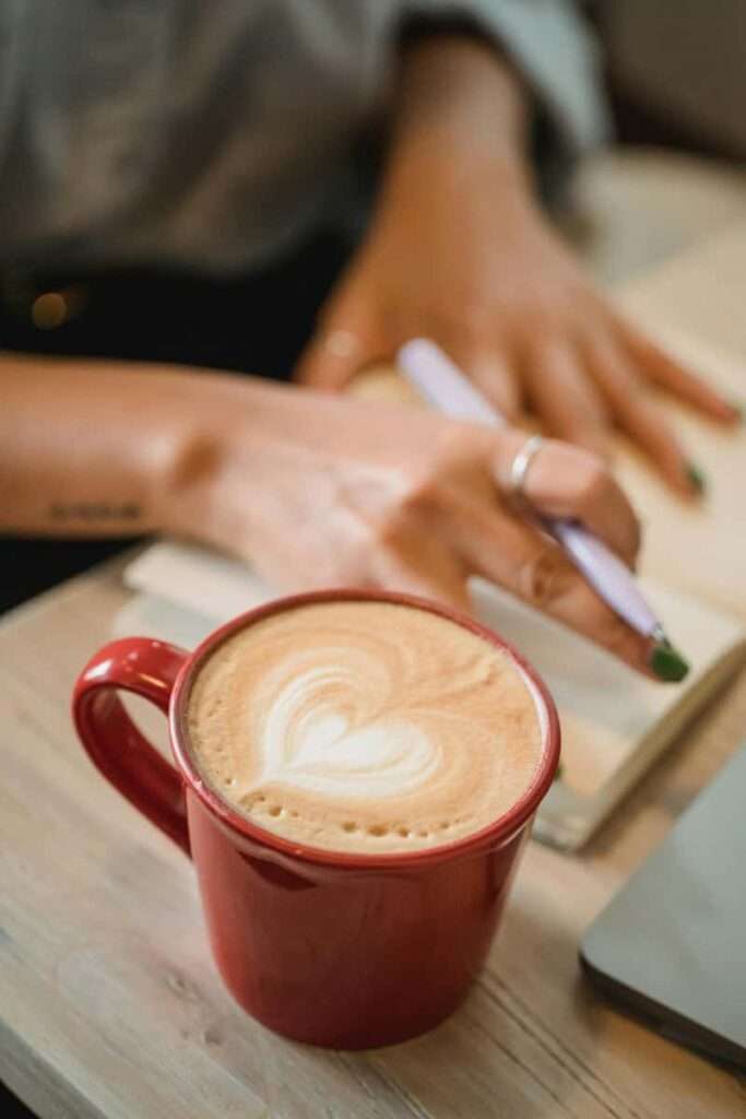 Image of a woman writing in her journal alongside sipping a cup of tea, representing the use of birthday journaling prompts.