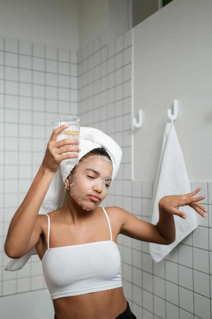 A woman doing skincare in her bathroom while nourishing her body with water, representing a soft Sunday reset self-care ritual.
