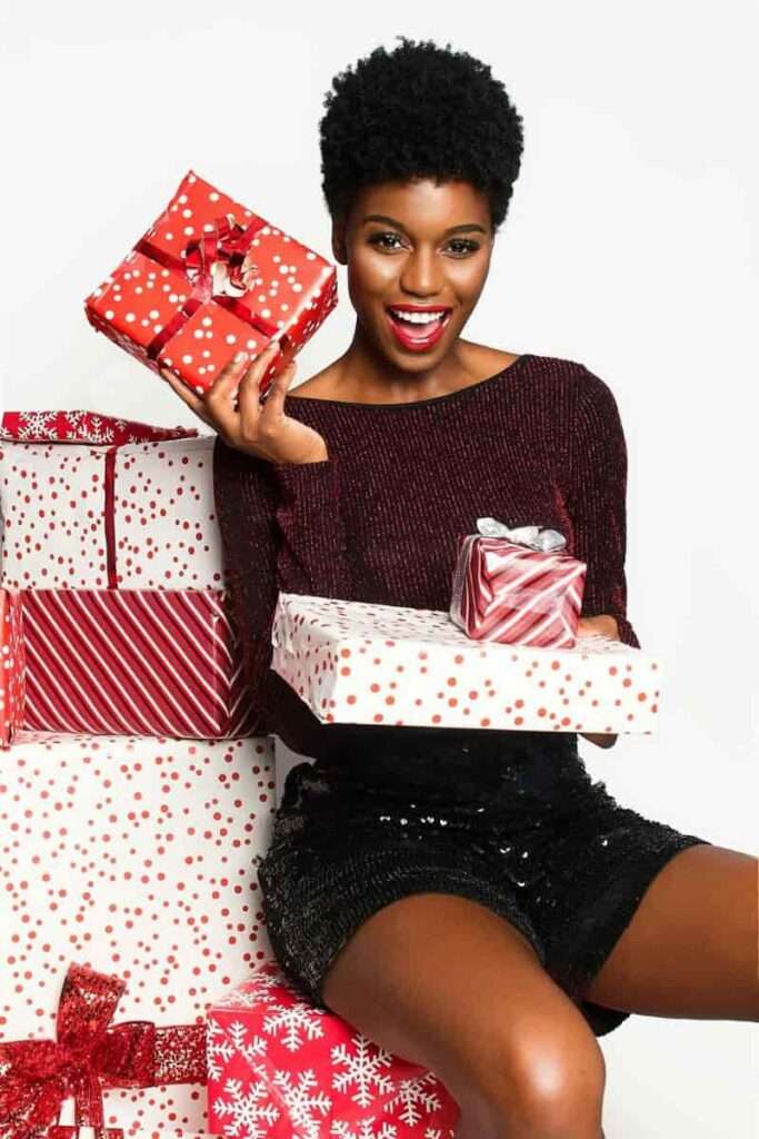 Black women with red sweaters surrounded by beautifully wrapped gifts, representing the end-of-year rituals such as gifting.